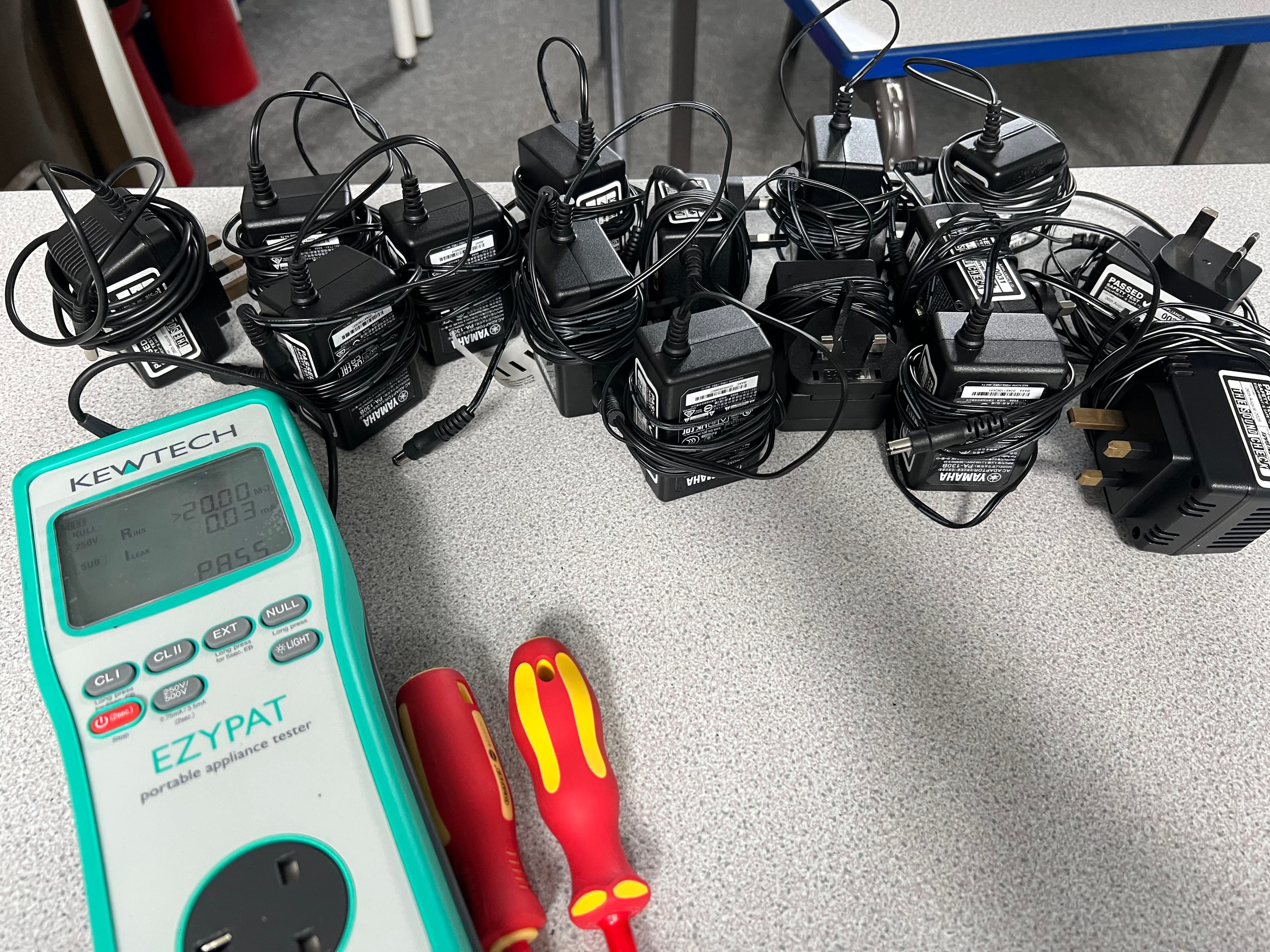 A portable PAT tester beside a collection of adapters and cables